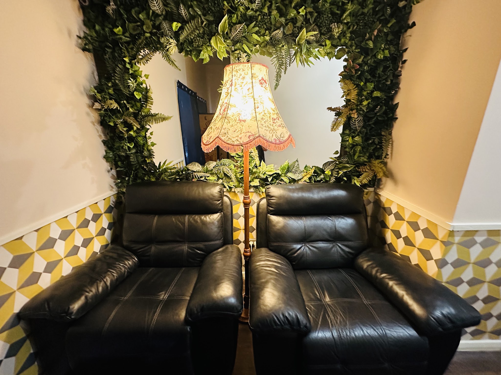 Two black leather recliners for foot reflexology beneath a leafy frame and a floral lamp