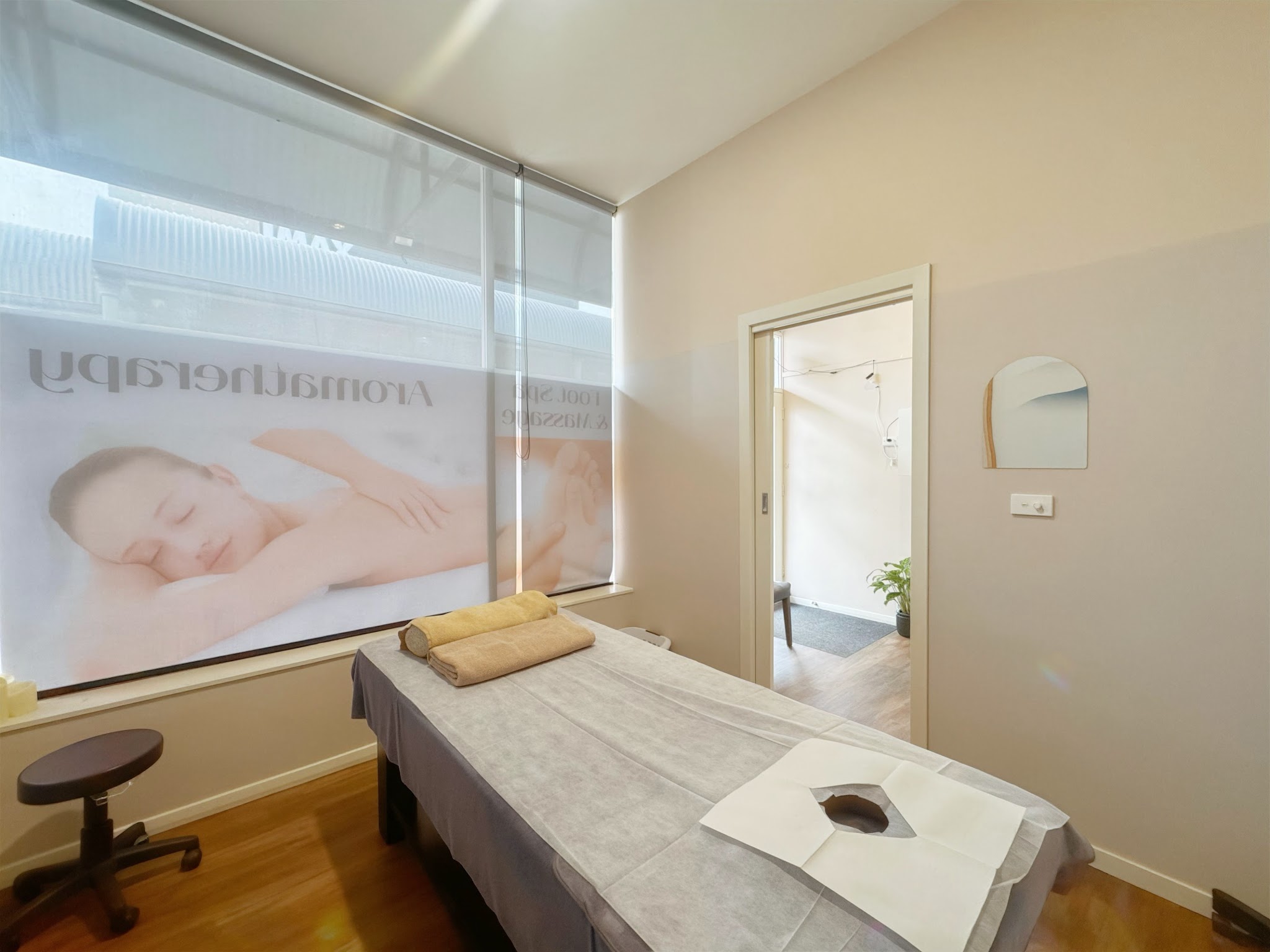A treatment room with a massage table, stool and the window blind drawn