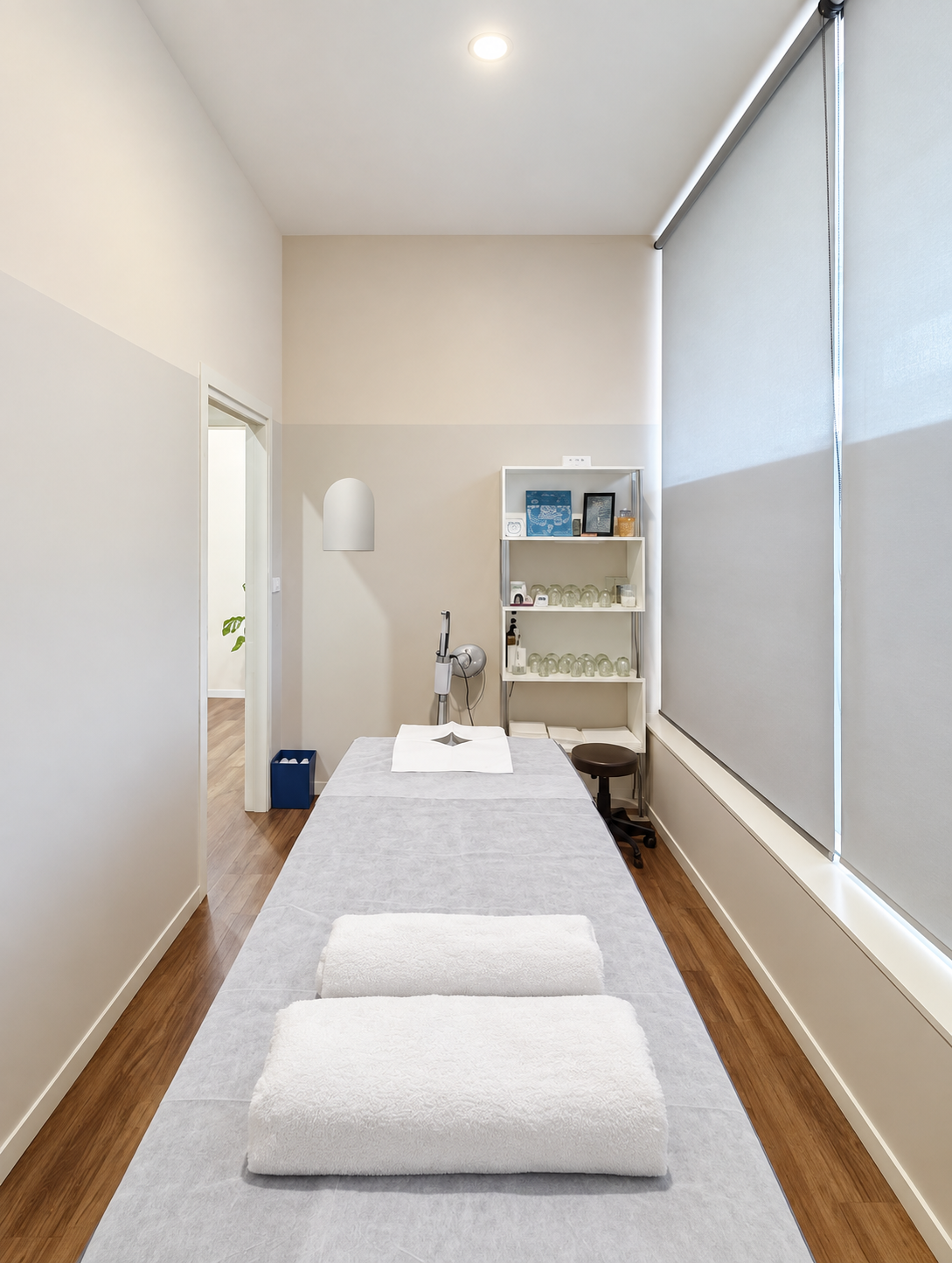 A narrow private treatment room with folded white towels on the table