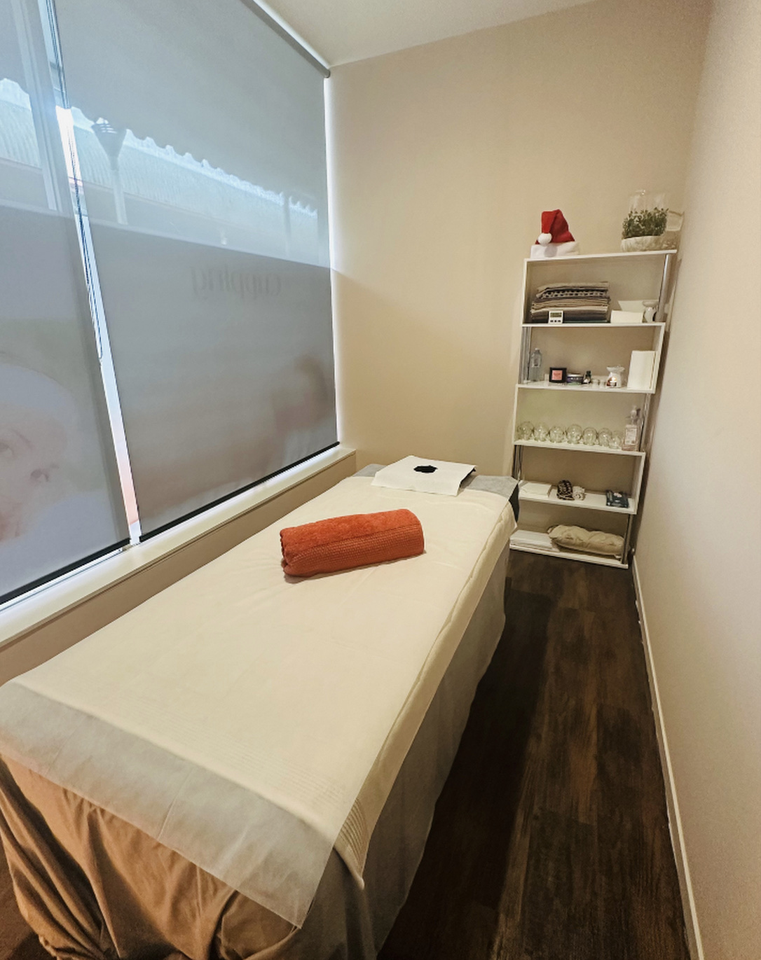 A treatment room with a massage table, an orange towel and a shelf of cupping jars